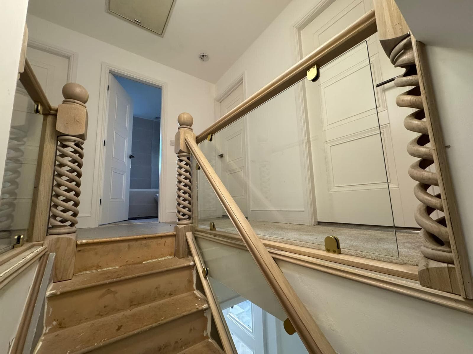 Open barley-twist oak newel post and glass balustrade rising over a staircase in a Yorkshire home