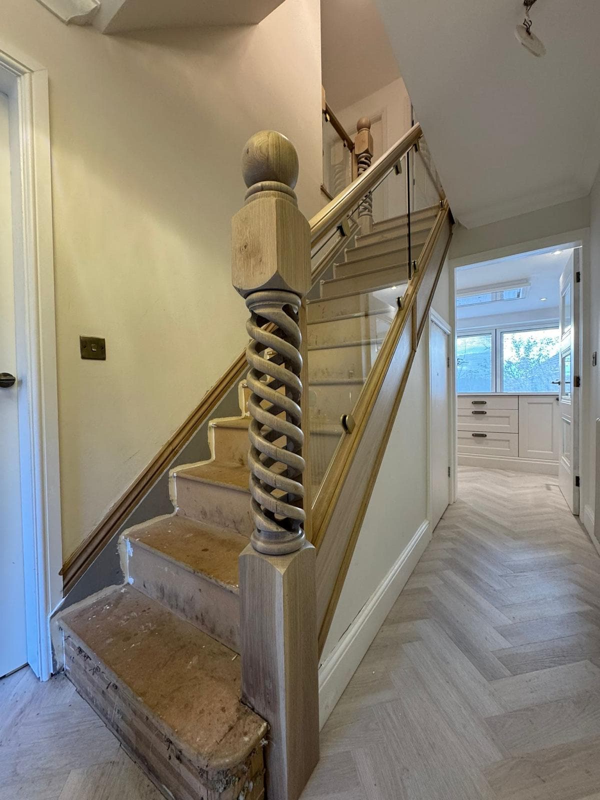 Hand-turned oak open-twist newel post at the foot of a staircase flight with a glass balustrade