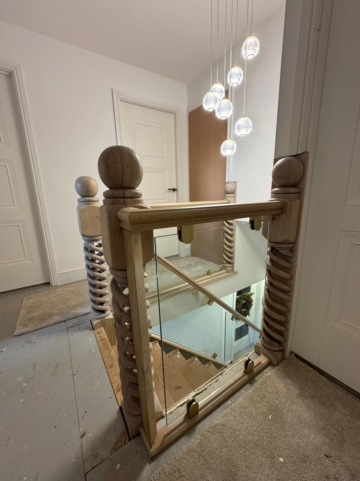 Oak barley-twist newel posts with ball-cap finials and a glass balustrade on a galleried landing, hand-turned by Spindles Woodturning